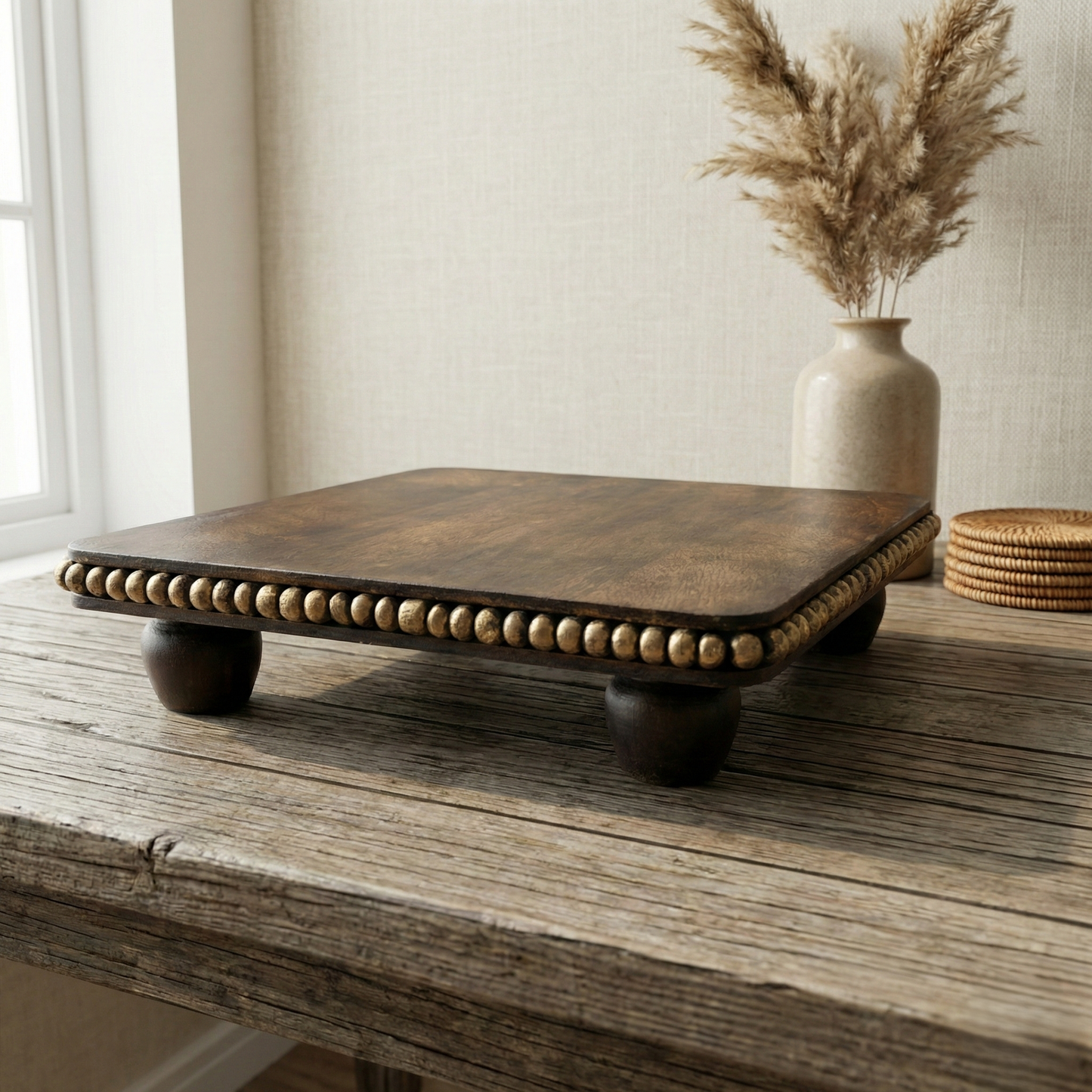 Handcrafted wooden decorative tray with brass bead accents on a rustic table