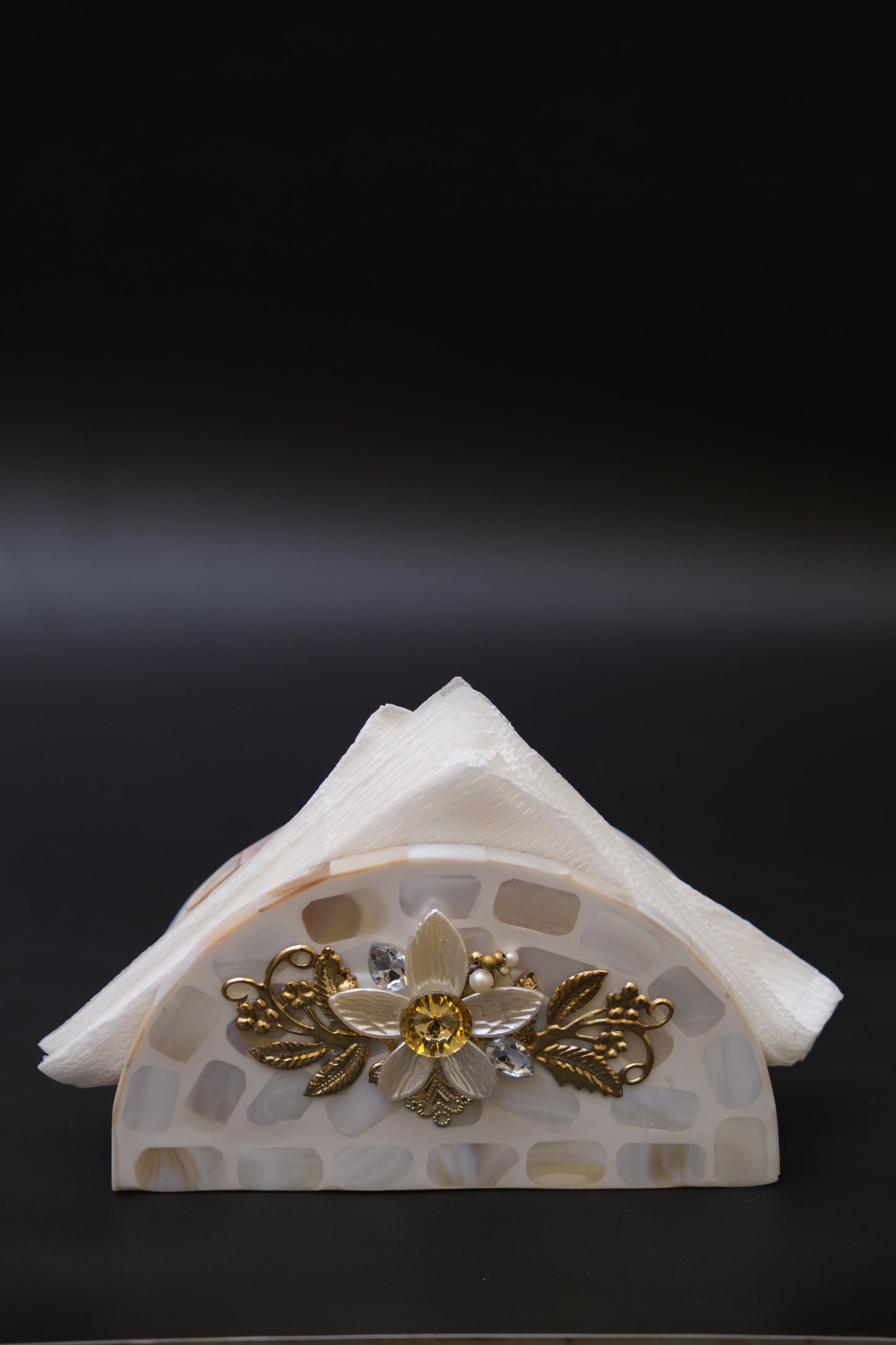 Handcrafted mother of pearl floral napkin holder with gold accents against black background