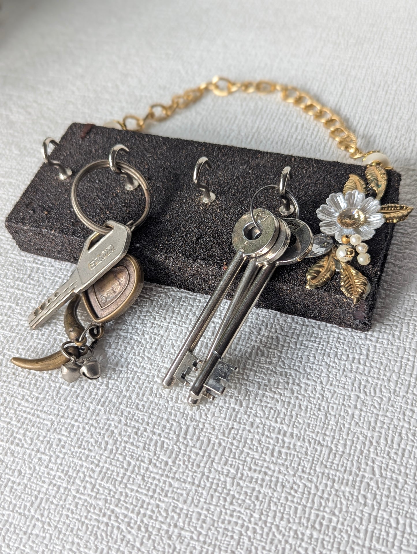 Handcrafted wooden key holder with metal hooks, floral accent, and gold chain on white surface