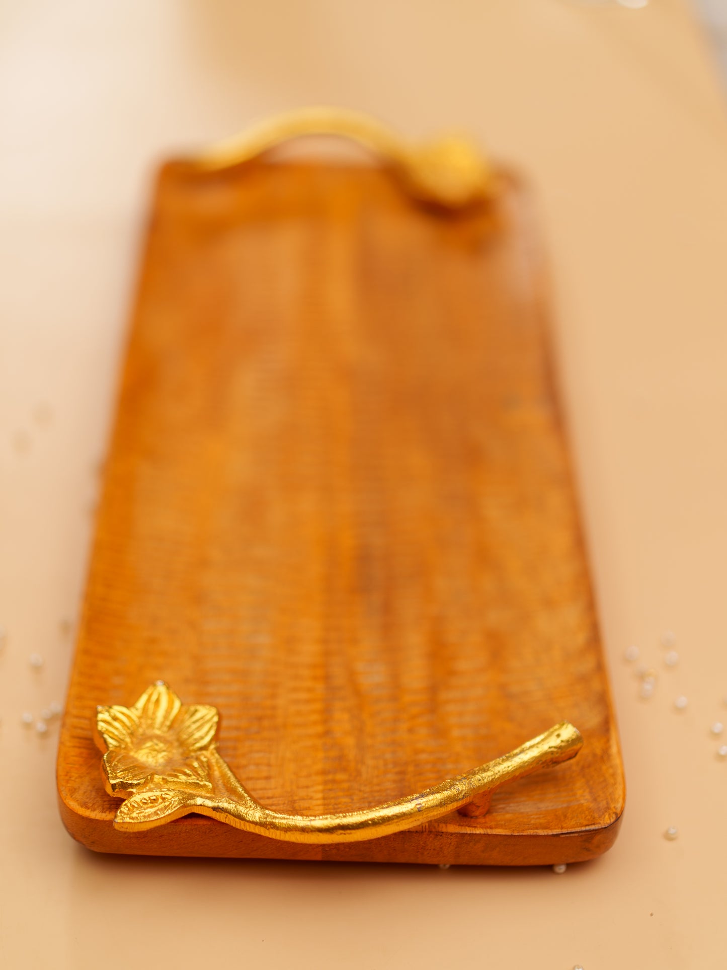 Rectangular wooden serving tray with gold floral handles on a beige surface