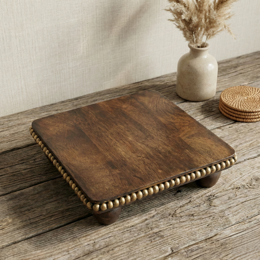 Handcrafted wooden decor platform with beaded trim on rustic table, vase and coasters nearby