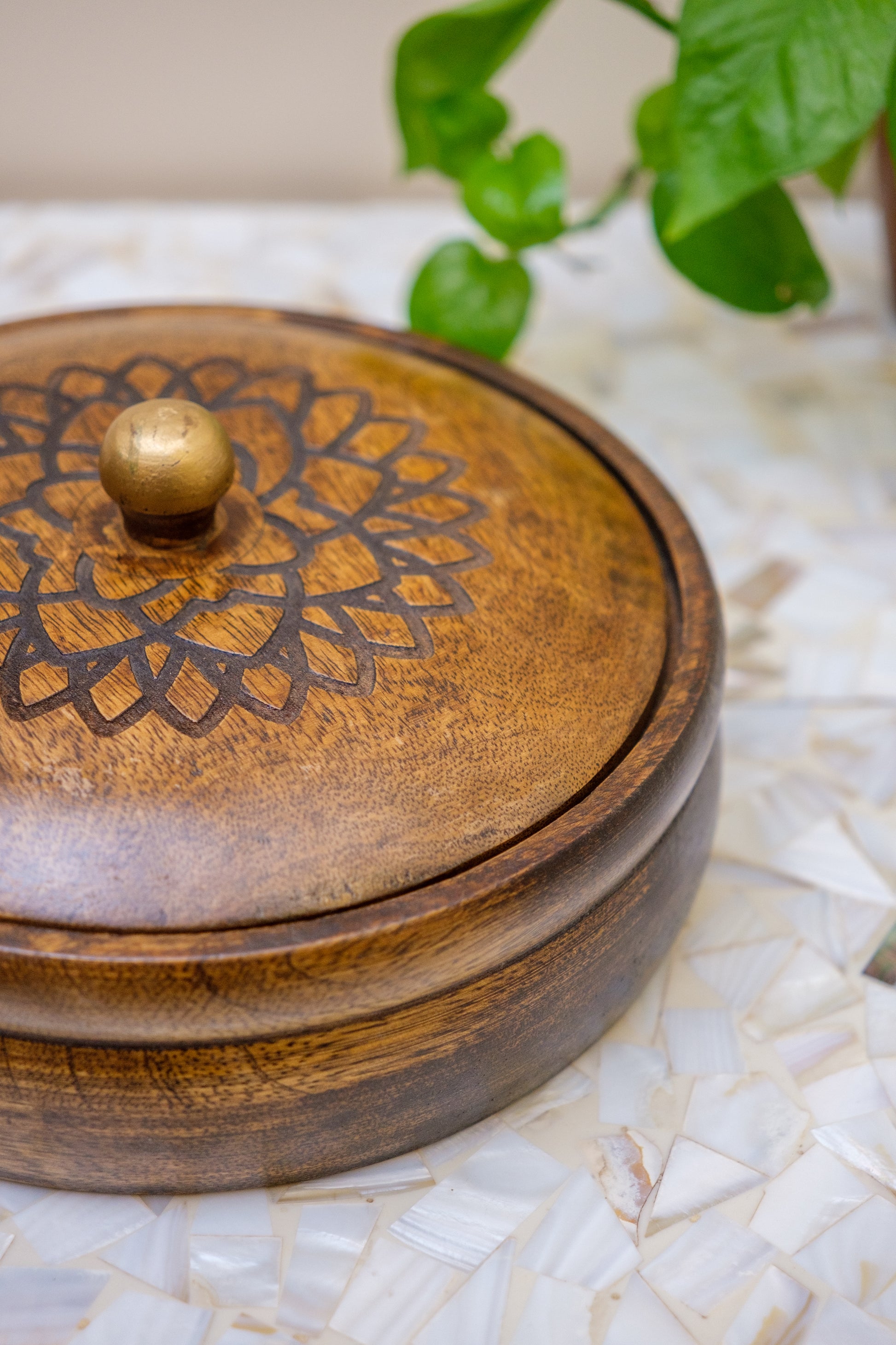 Handcrafted wooden box with etched floral pattern and brass knob, on mosaic table