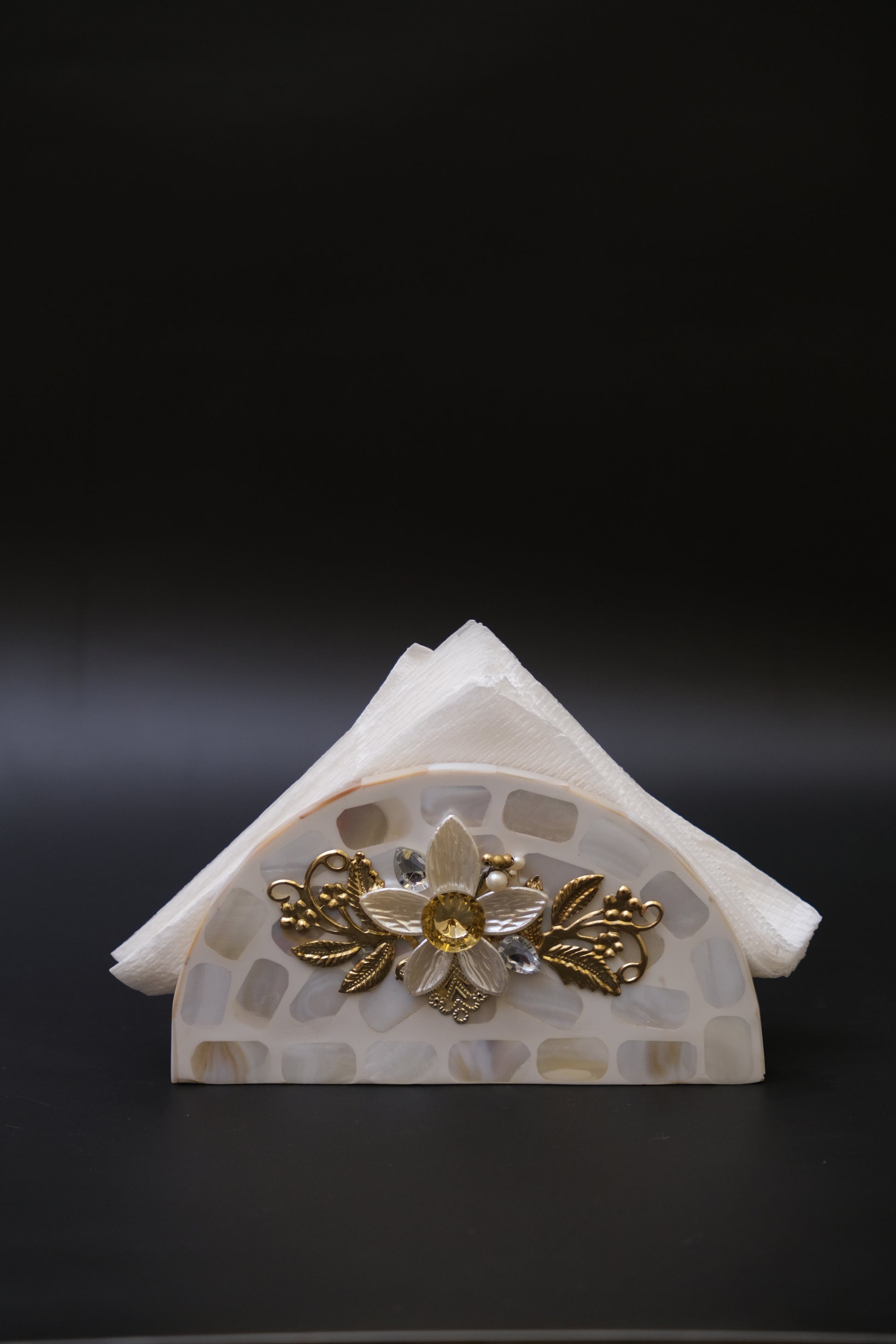 Mother of pearl napkin holder with floral and gold accents on a black background