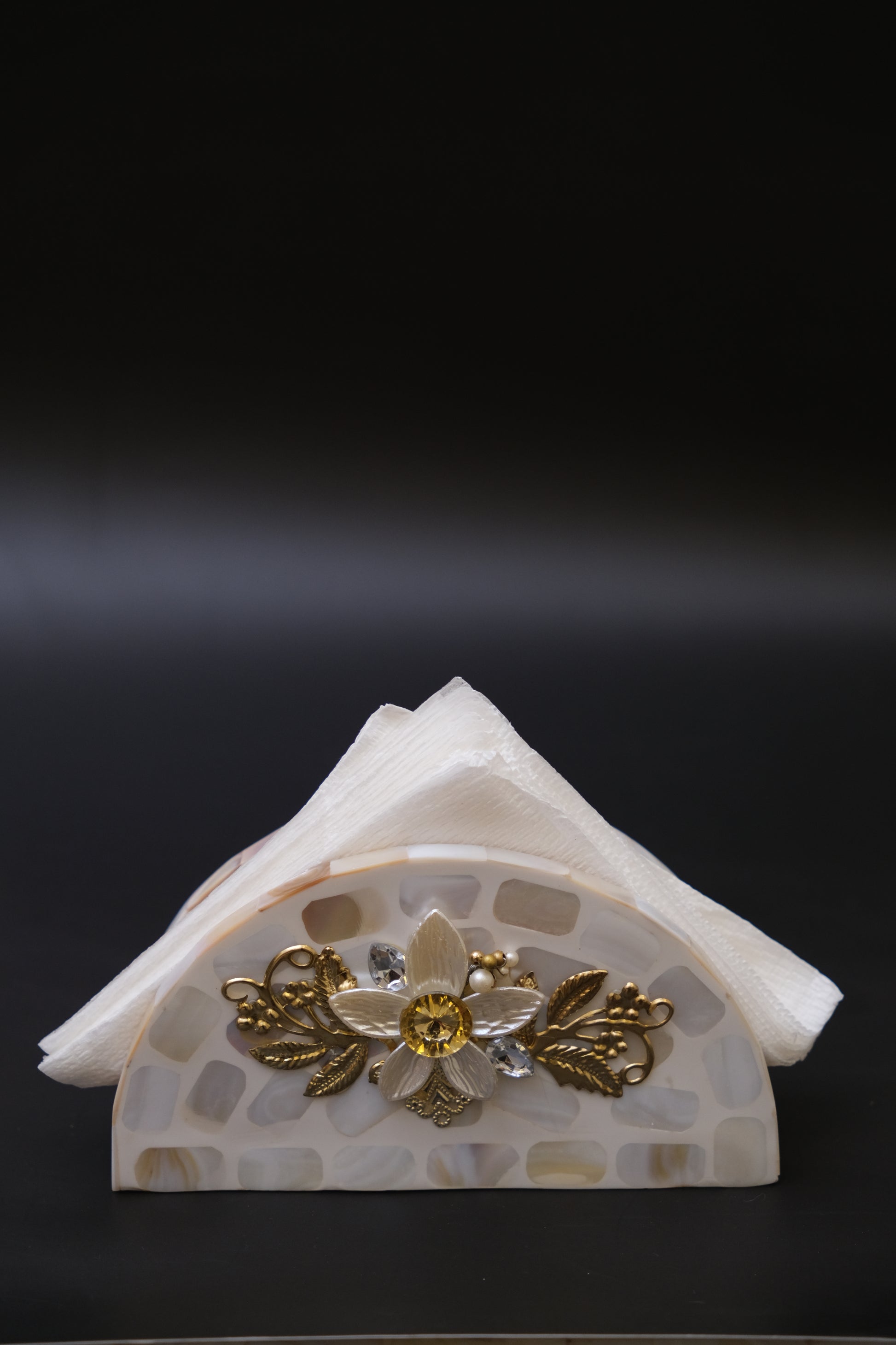 Handcrafted mother of pearl floral napkin holder with gold accents against black background