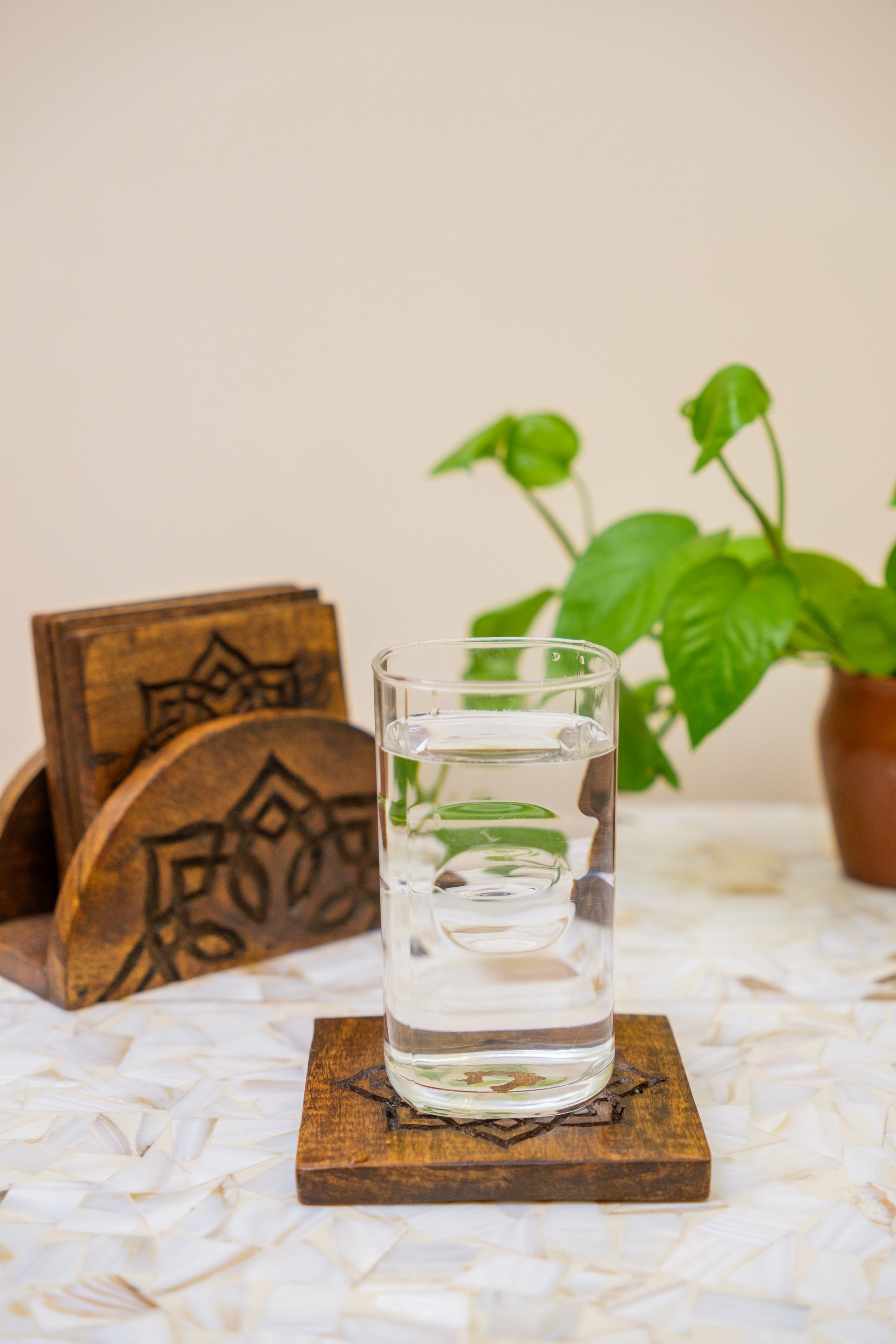Handcrafted wooden coaster set with carved design, glass of water, and green plant