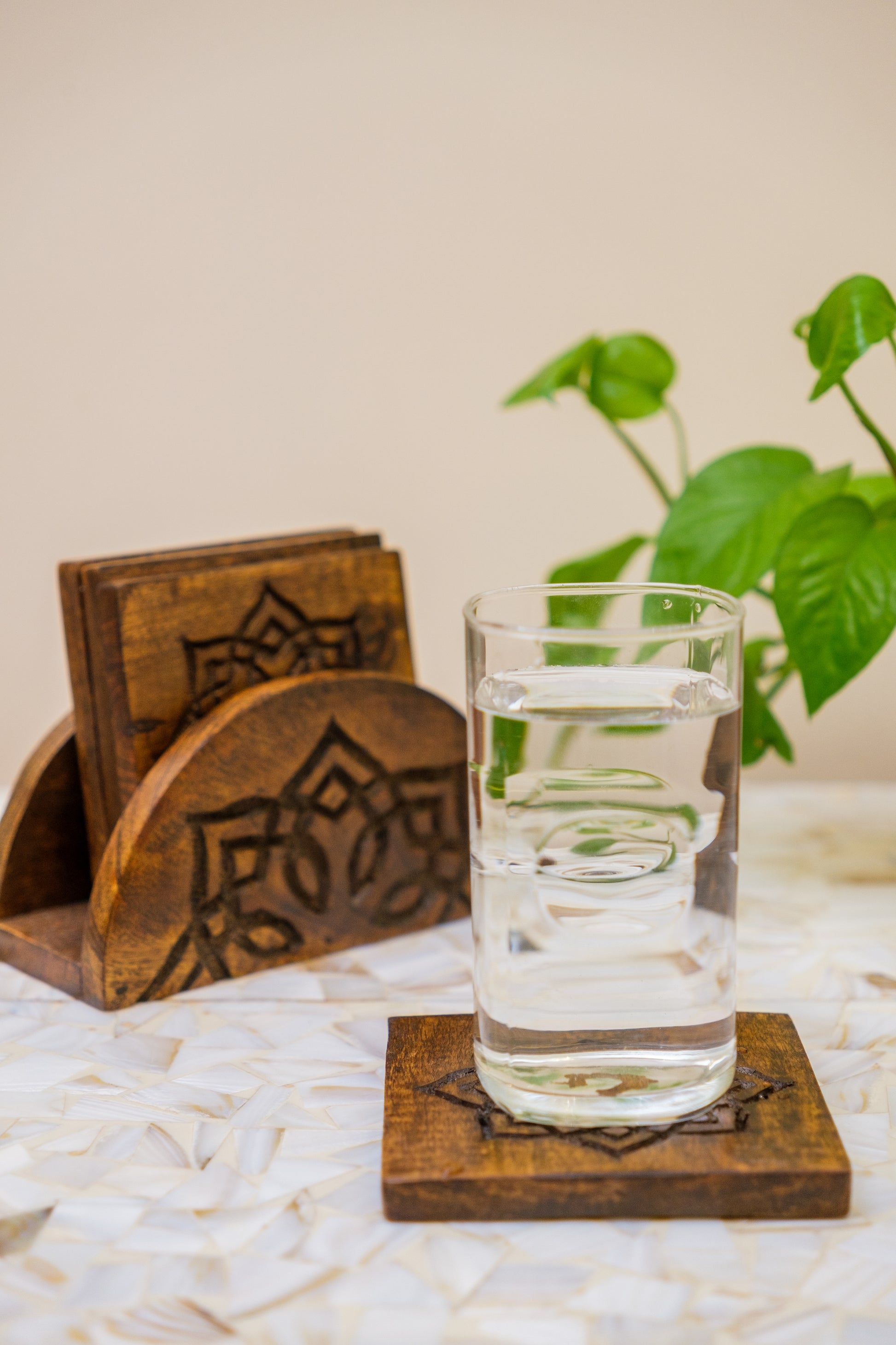Handcrafted wooden coasters with engraved floral pattern, glass of water, and green plant