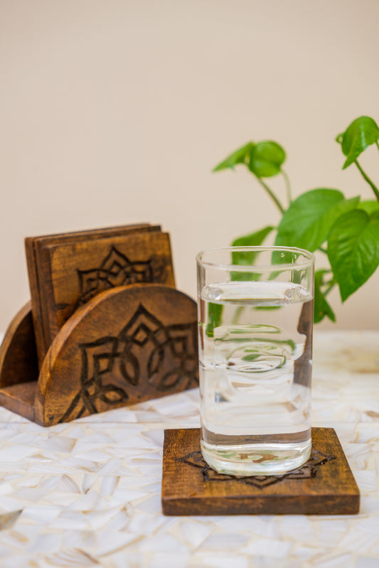 Handcrafted wooden coasters with engraved floral pattern, glass of water, and green plant