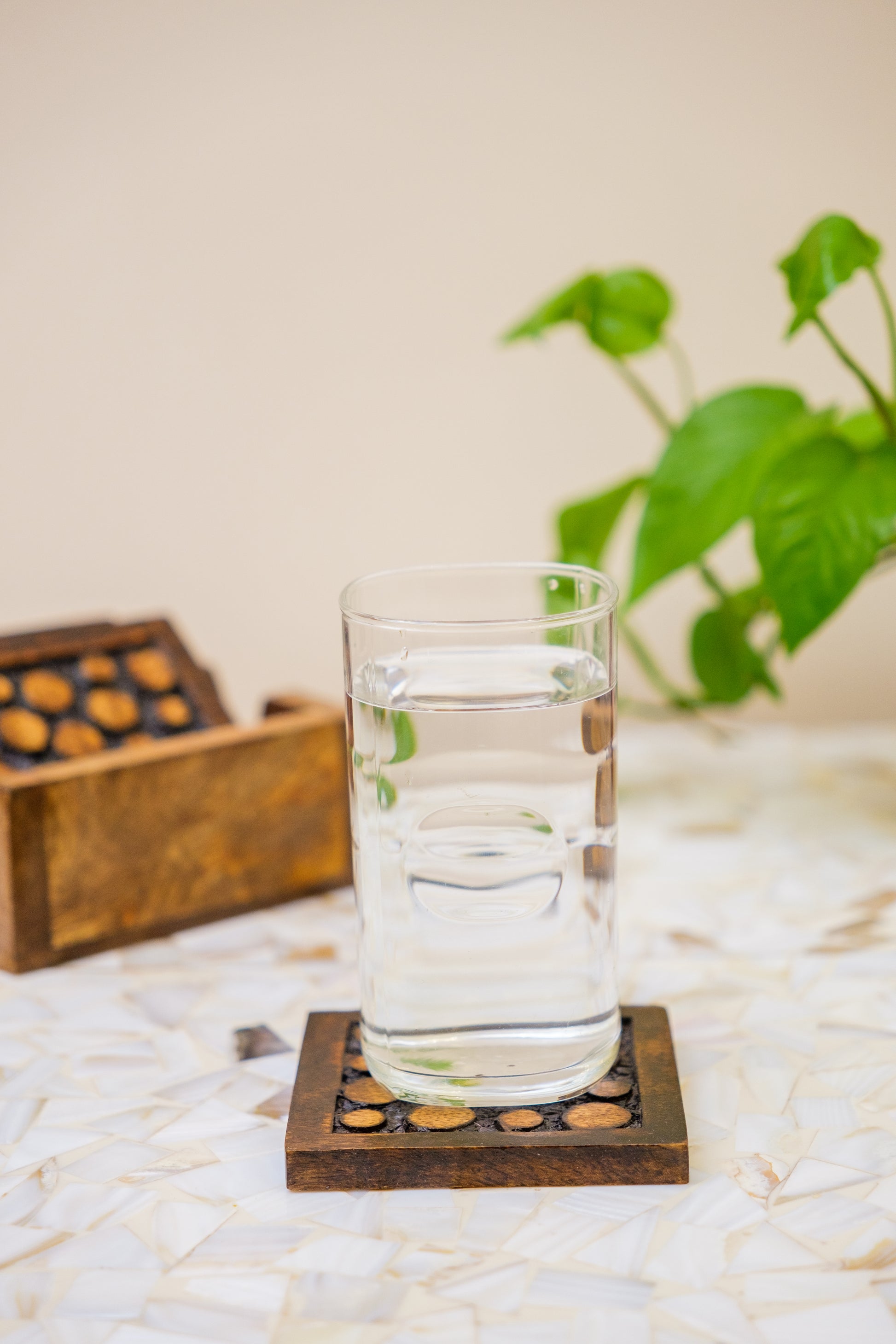 Glass of water on handcrafted wooden coaster with inlay, decorative box and plant in background