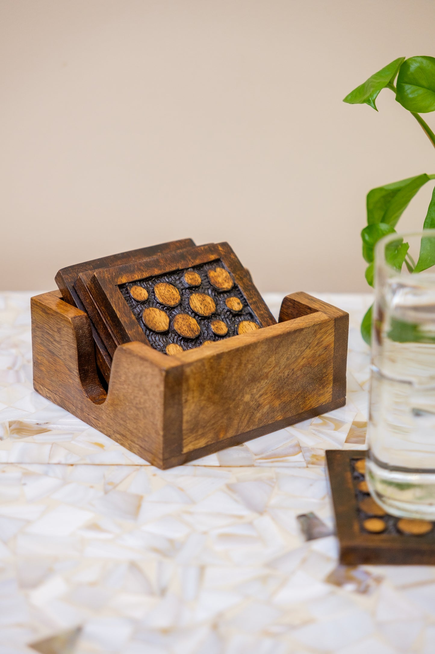 Handcrafted wooden coasters with carved dot design in holder on marble table