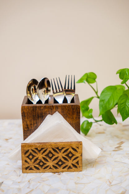 Handcrafted wooden cutlery and napkin holder with carved floral design, silverware, and plant decor