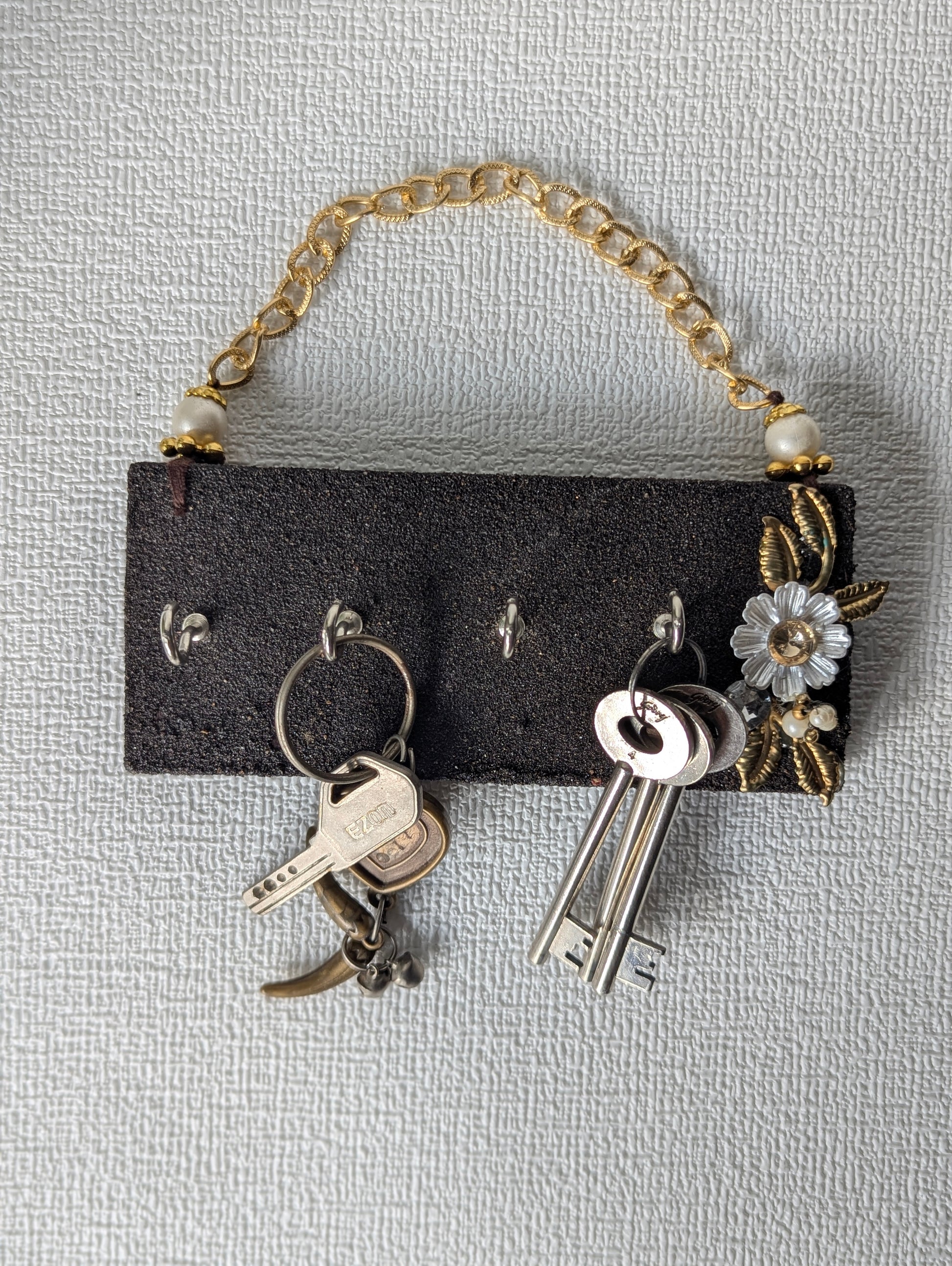 Handcrafted wooden key holder with gold chain, floral embellishments, and keys hanging