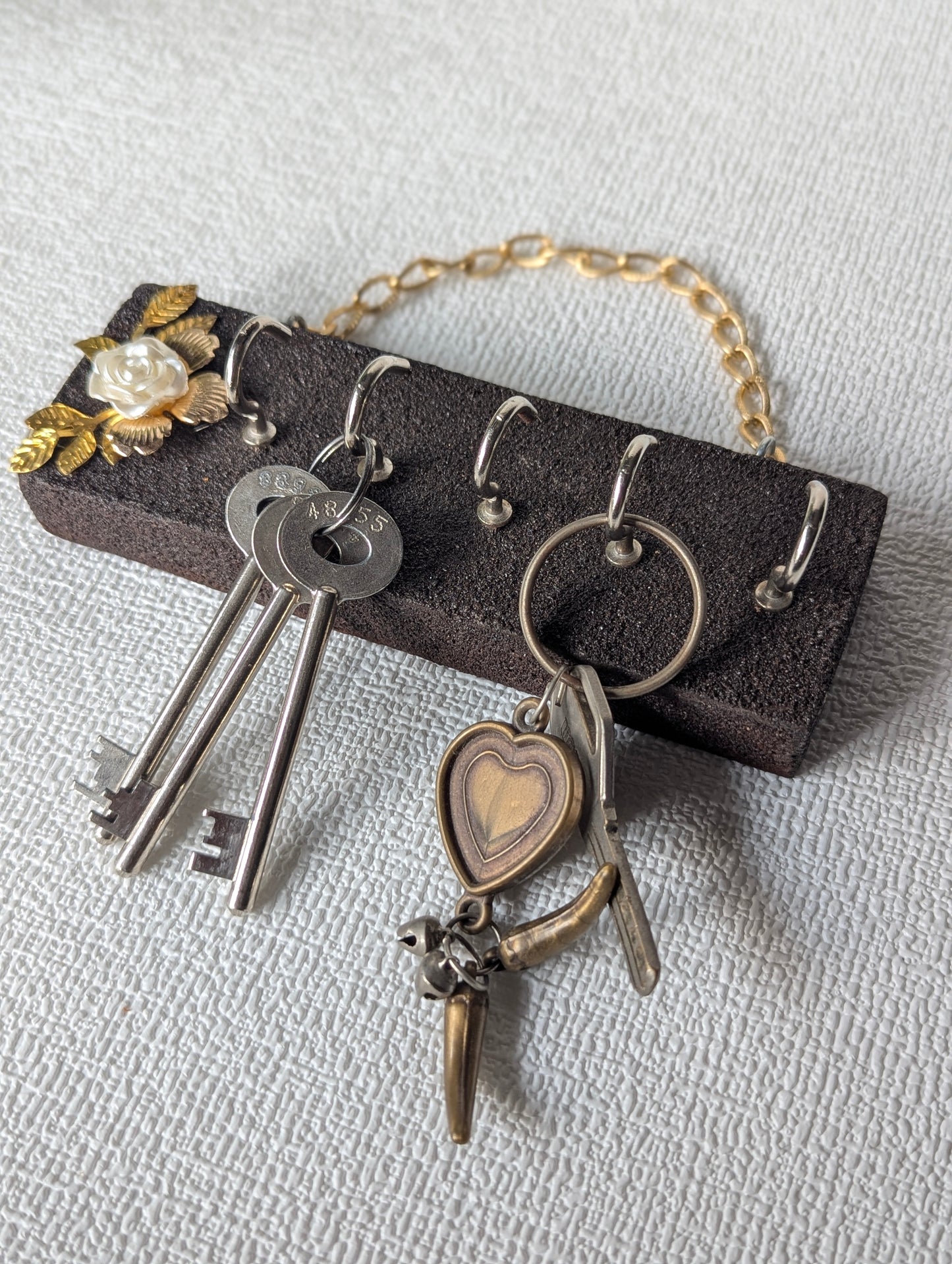 Handcrafted wooden key holder with gold chain, white floral accent, and vintage keys