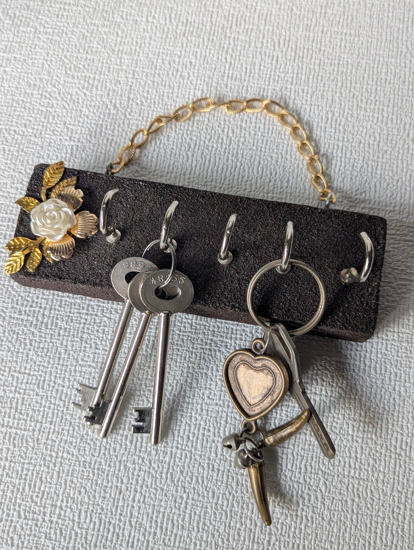 Handcrafted wooden key holder with floral design, hanging on textured wall, holding keys