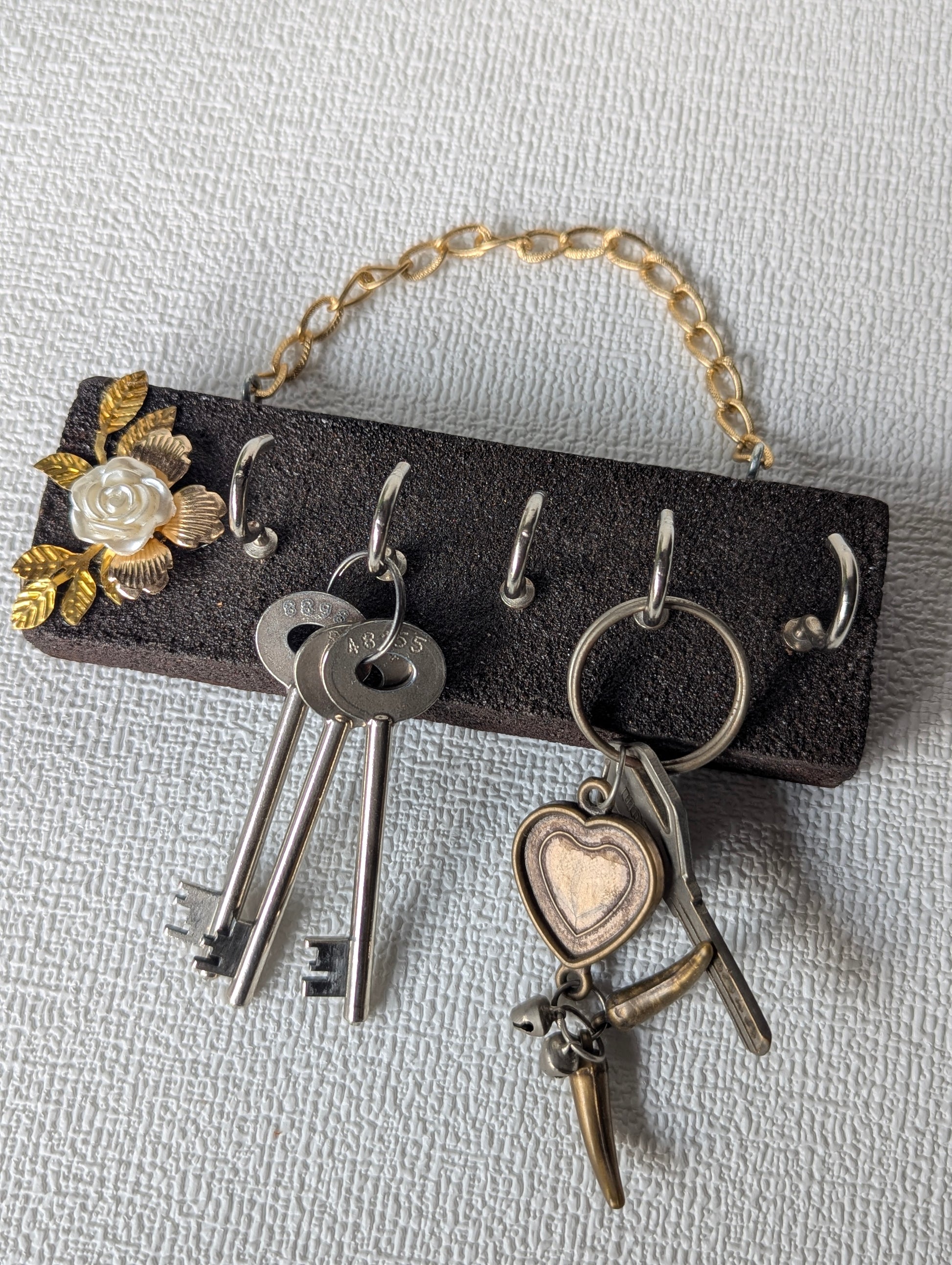 Handcrafted wooden key holder with floral design, hanging on textured wall, holding keys
