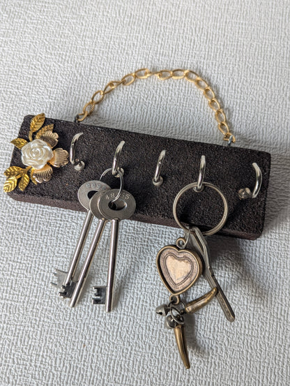Handcrafted wooden key holder with floral design, hanging on textured wall, holding keys