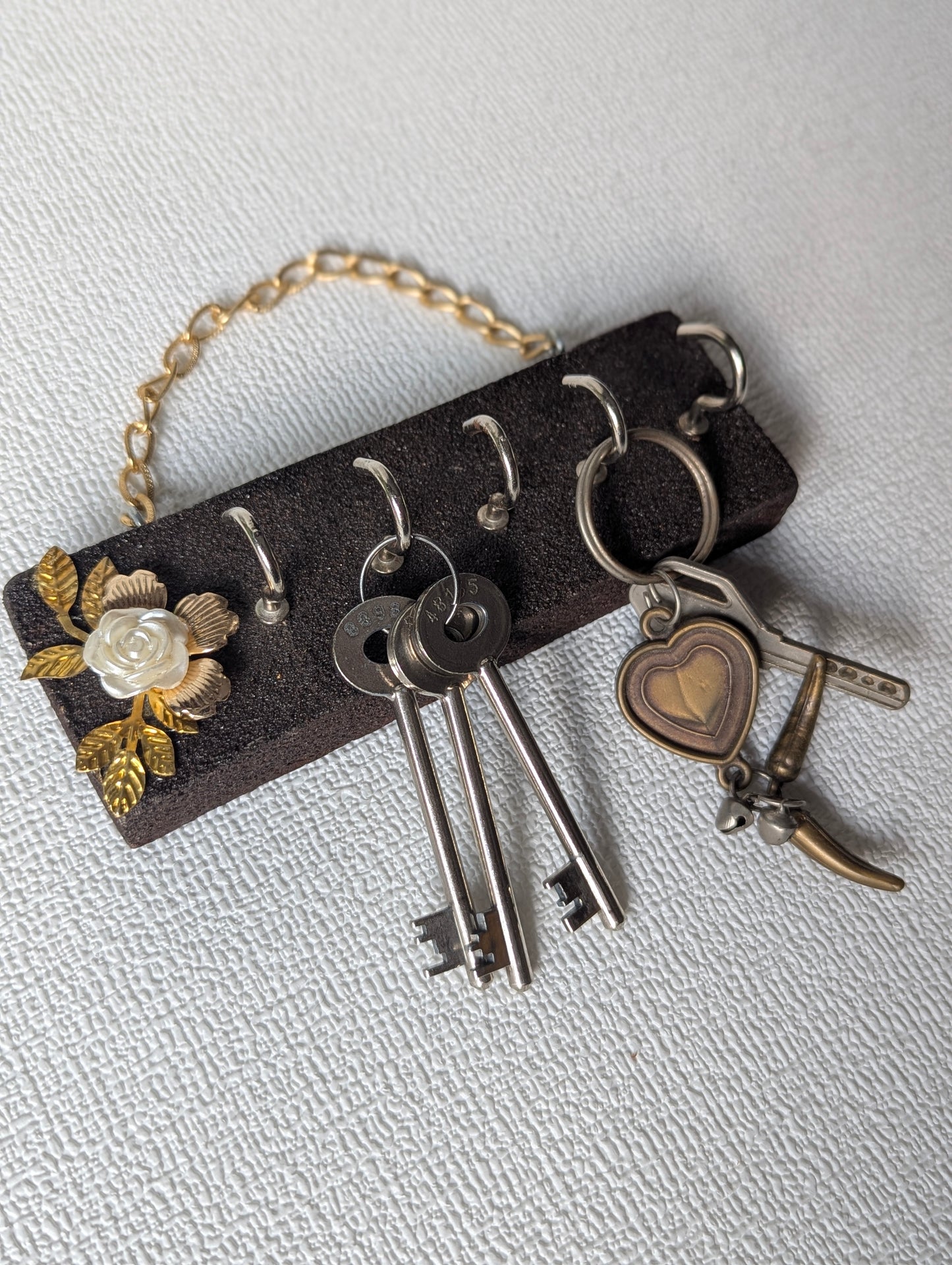 Handcrafted wooden key holder with white flower and gold leaf decor, holding keys.