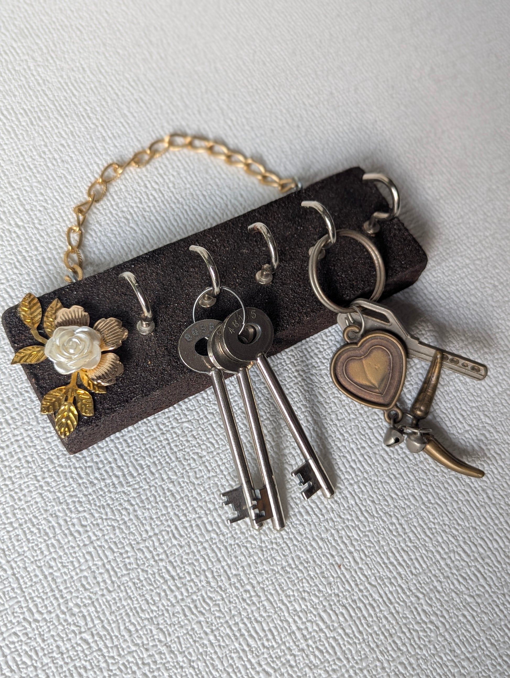 Handcrafted wooden key holder with white flower and gold leaf decor, holding keys.