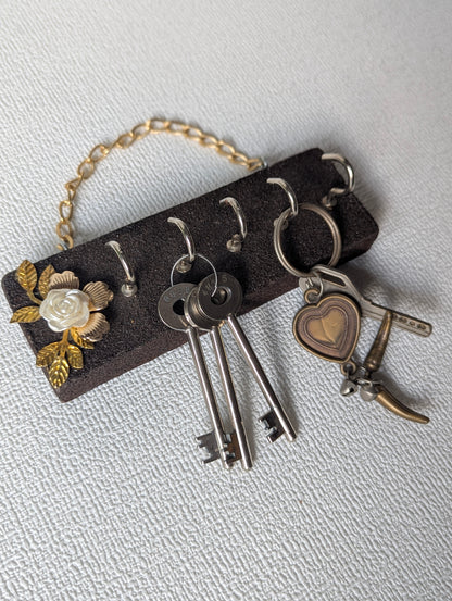 Handcrafted wooden key holder with white flower and gold leaf decor, holding keys.