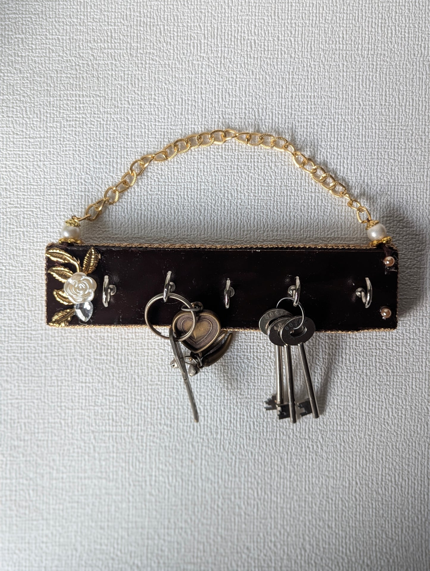 Handcrafted wooden key holder with floral inlay, gold chain, and multiple keys hanging