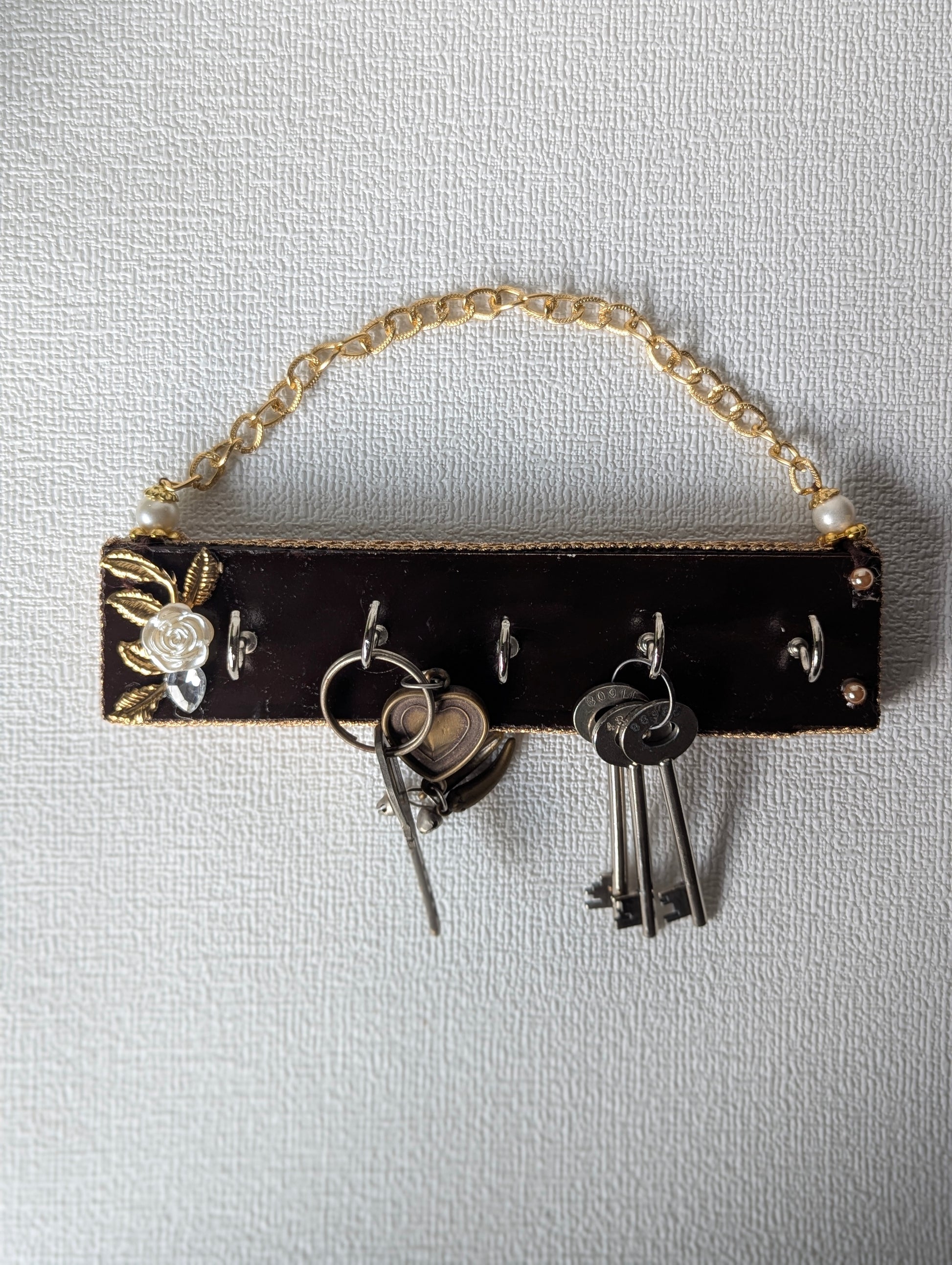 Handcrafted wooden key holder with floral inlay, gold chain, and multiple keys hanging
