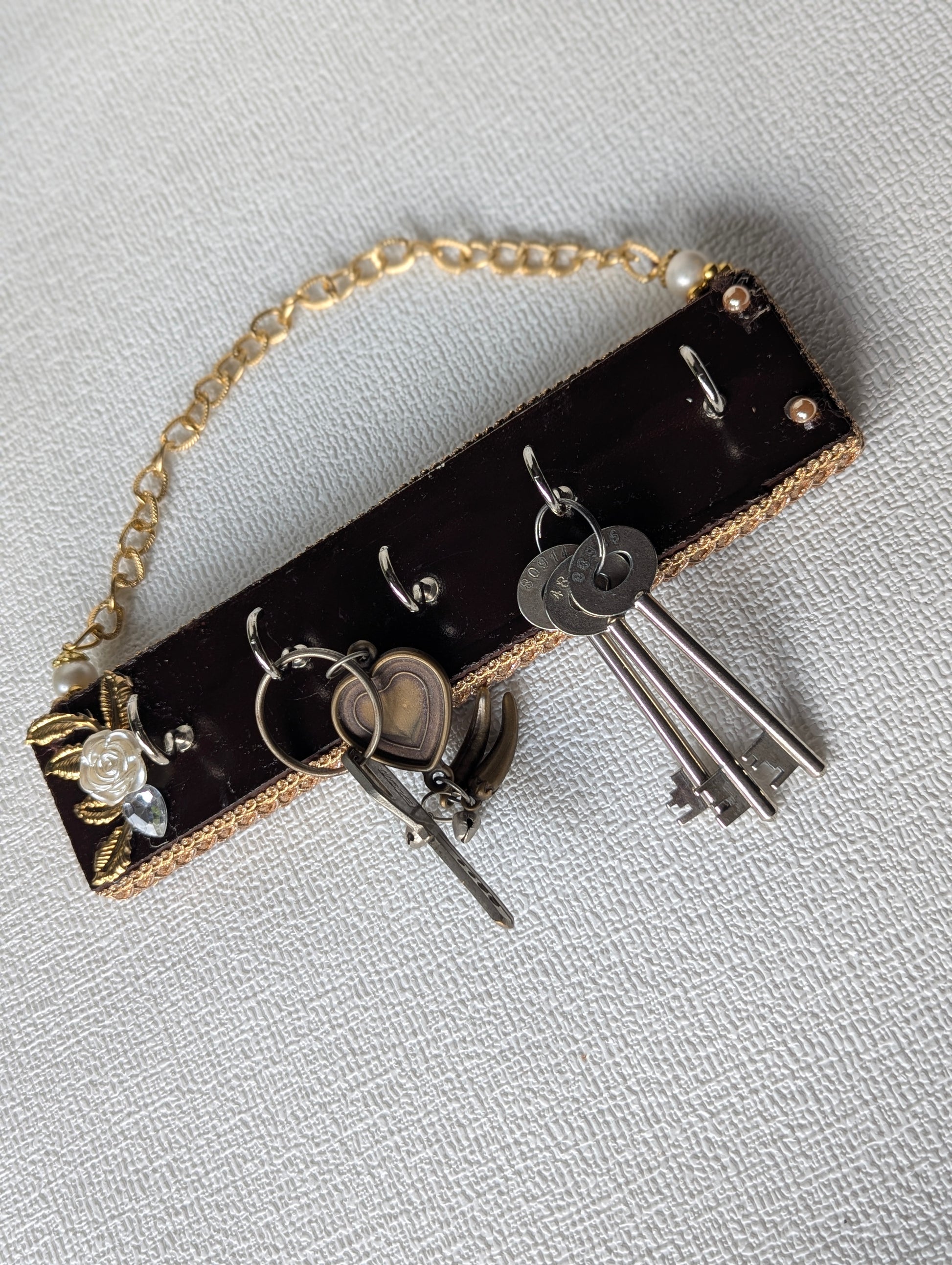 Handcrafted wooden key holder with gold floral accents, holding metal keys, on textured background