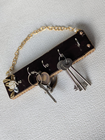 Handcrafted wooden key holder with gold floral accents, holding metal keys, on textured background