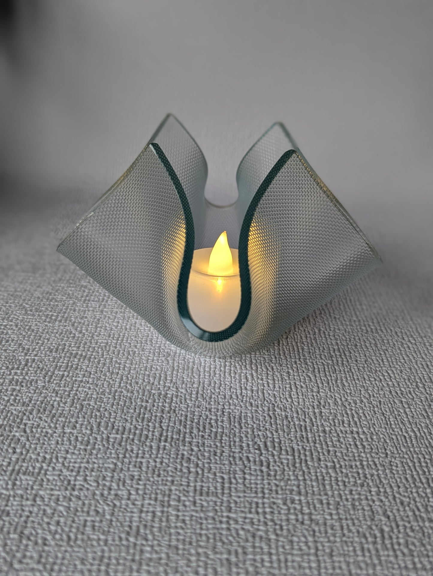 Handcrafted glass tealight holder with lit LED candle on textured white surface