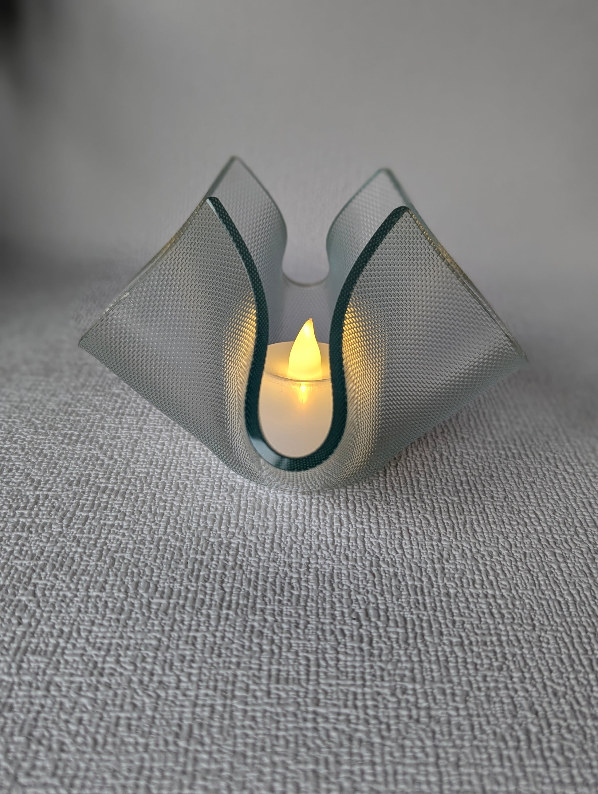 Handcrafted glass tealight holder with lit LED candle on textured white surface