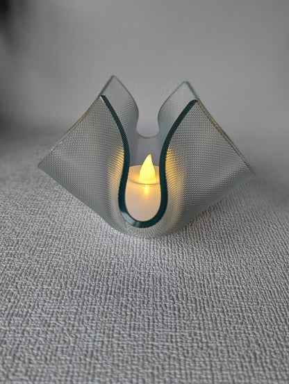 Handcrafted glass tealight holder with lit LED candle on textured white surface