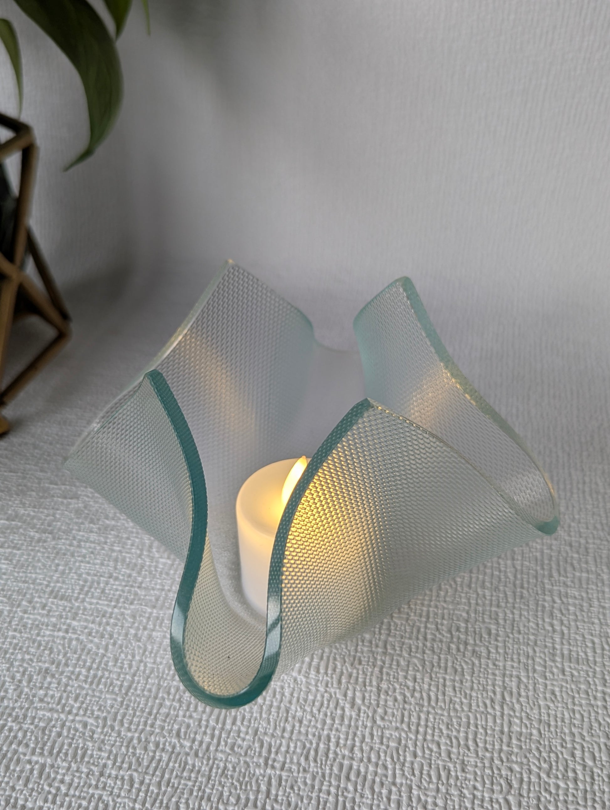 Handcrafted textured glass tealight holder with LED candle on white fabric surface