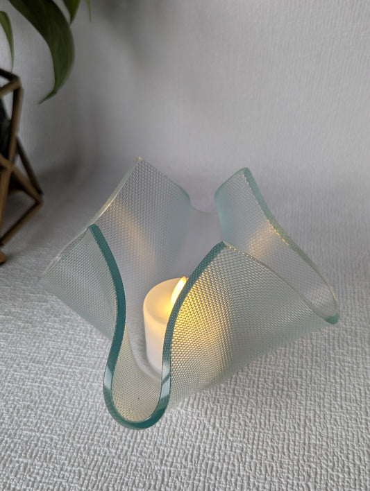 Handcrafted textured glass tealight holder with LED candle on white fabric surface
