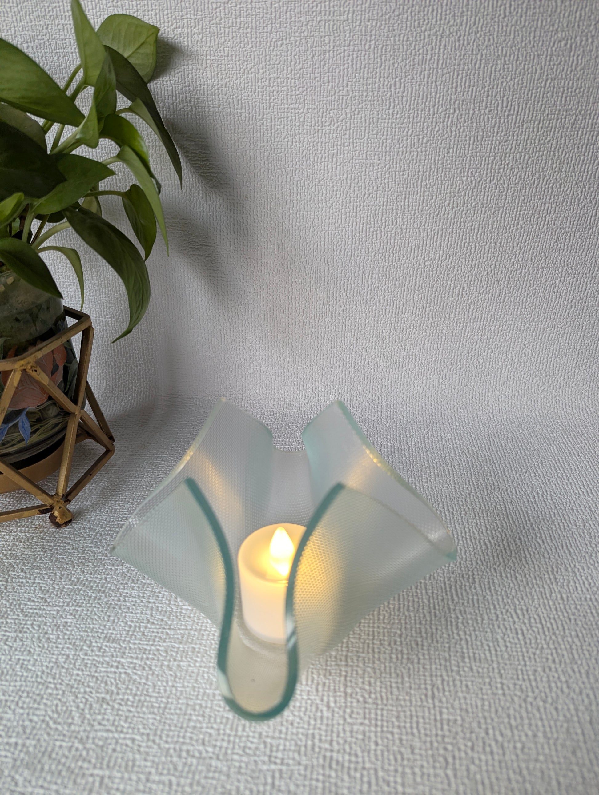 Glass tealight candle holder with flameless LED candle and potted plant on textured surface