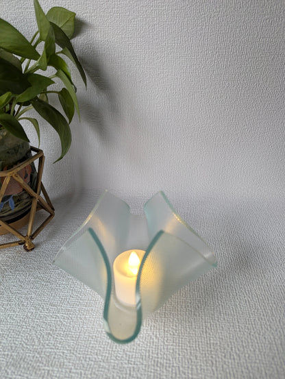Glass tealight candle holder with flameless LED candle and potted plant on textured surface