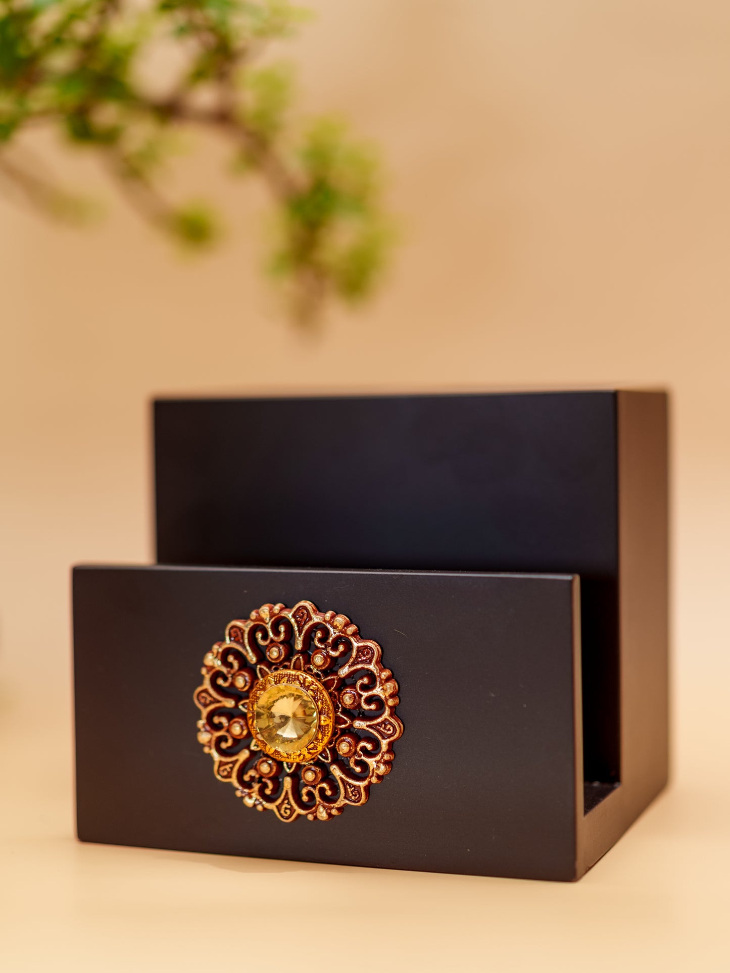 Black wooden napkin holder with ornate gold floral design and gemstone accent
