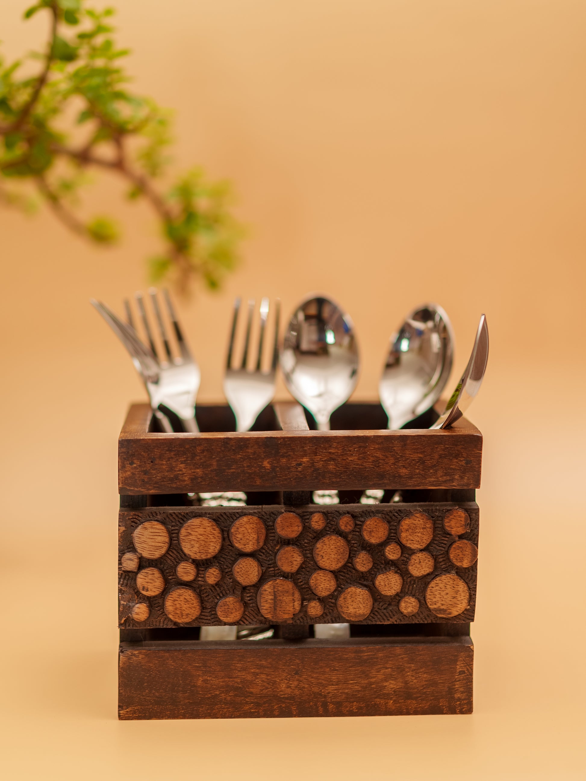 Handcrafted wooden cutlery holder with textured circles, filled with silverware on beige background