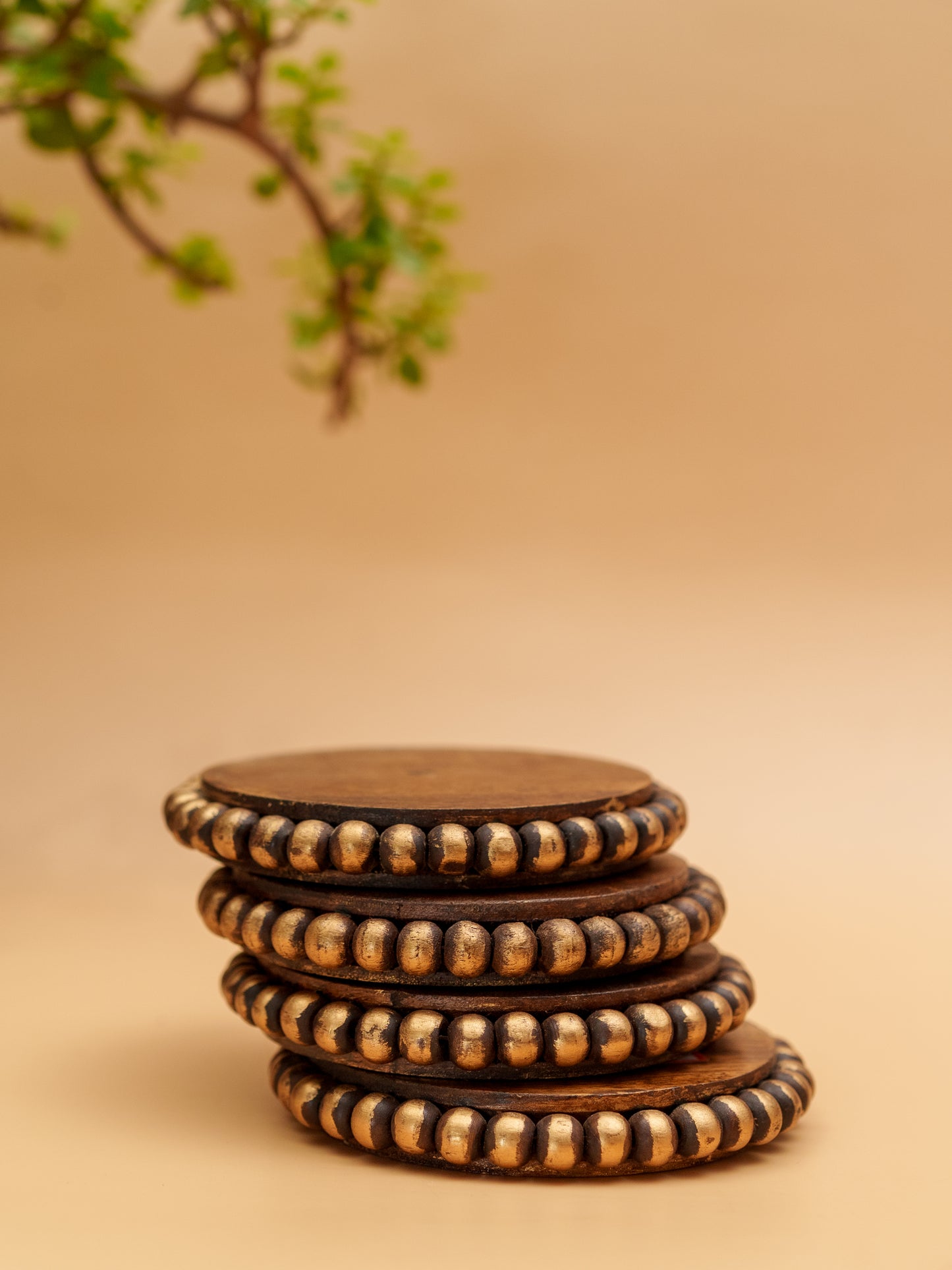 Stack of handcrafted wooden coasters with gold beaded edges on beige background