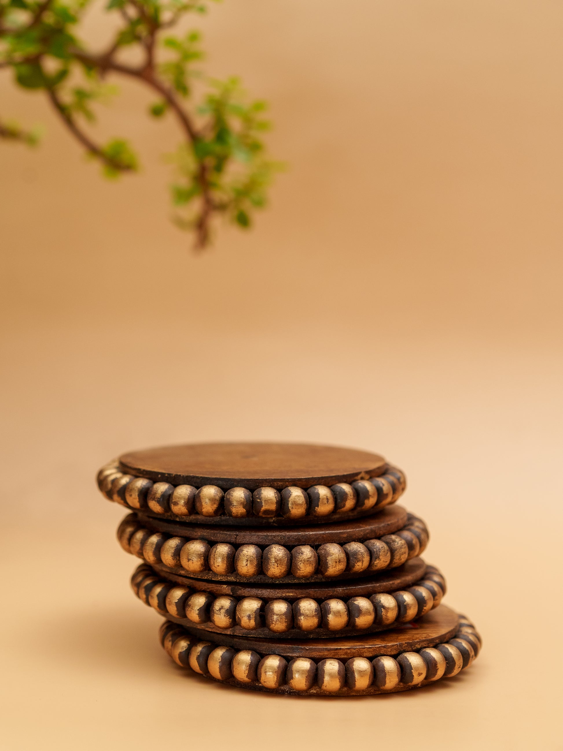 Stack of handcrafted wooden coasters with gold beaded edges on beige background