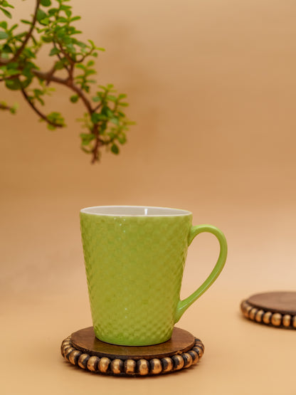 Green textured ceramic mug on beaded wooden coaster, with plant and neutral background