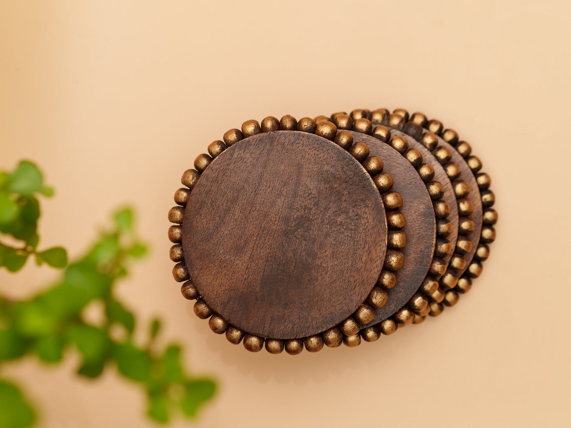 Set of round wooden coasters with gold beaded edge on beige background, home decor